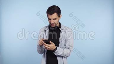 穿着蓝色t恤、脖子上戴着耳机的英俊、好奇的男人展示了智能手机和绿色屏幕智能手机